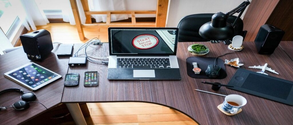 Bureau moderne avec divers appareils électroniques et un ordinateur portable affichant 'START ENGINE STOP'.